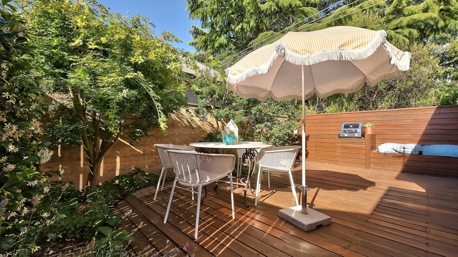 Une terrasse en bois avec une table et des chaises, un barbecue et un mur en bois agrémenté d’un banc.
