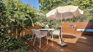 Une terrasse en bois avec une table et des chaises, un barbecue et un mur en bois agrémenté d’un banc.