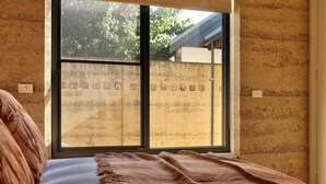 Ein Zimmer mit großem Fenster, einem Bett mit brauner Decke und einer Wand mit strukturierter Oberfläche.