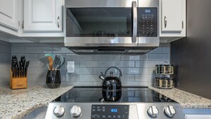Una cucina con forno a microonde, forno e piano cottura in acciaio inox. Ci sono coltelli in un portacoltelli di legno, un bollitore e barattoli di spezie sul piano di lavoro.