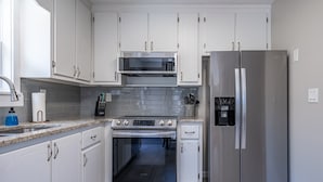Una cucina moderna con mobili bianchi, elettrodomestici in acciaio inossidabile tra cui microonde, forno e frigorifero, un piano di lavoro in granito e un dispenser per l'acqua.