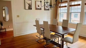 Zona pranzo con tavolo di legno e sei sedie, un lampadario e quadri appesi alle pareti.