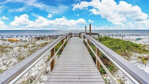 Een houten looppad naar een strand met parasols en ligstoelen.