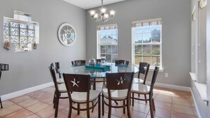 Un coin repas comprenant une table ronde en verre, six chaises et un lustre.