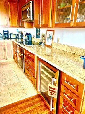 A kitchen with wooden cabinets, a stainless steel microwave, and a granite countertop. - Peaceful 3-bedroom bungalow in enchanting Kailua-Kona perfect for relaxing (Kailua-Kona)