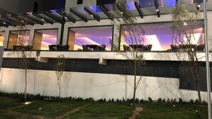 A modern building with a flat roof, large windows, and a covered outdoor area with seating. - 2-bedroom apartment close to comercial area and industrial zones (Qro.)