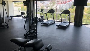 A gym with exercise equipment, a bench, treadmills, and a view of a residential area through large windows. - 2-bedroom apartment close to comercial area and industrial zones (Qro.)