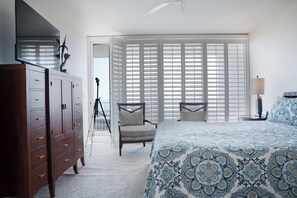 Quarto com cama grande, penteadeira, uma cadeira e varanda com vista.