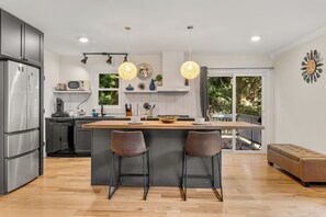 A modern kitchen with a central island, two bar stools, stainless steel appliances, and pendant lighting. - Rustic Elegance Surrounded by Nature (Raleigh)