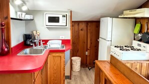 Una cucina compatta con mobili in legno, un piano di lavoro rosso, un forno a microonde, un fornello e un cestino.