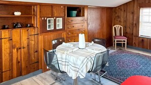 Zona pranzo con tavolo rotondo, sedie, un pensile in legno e una finestra con persiane.