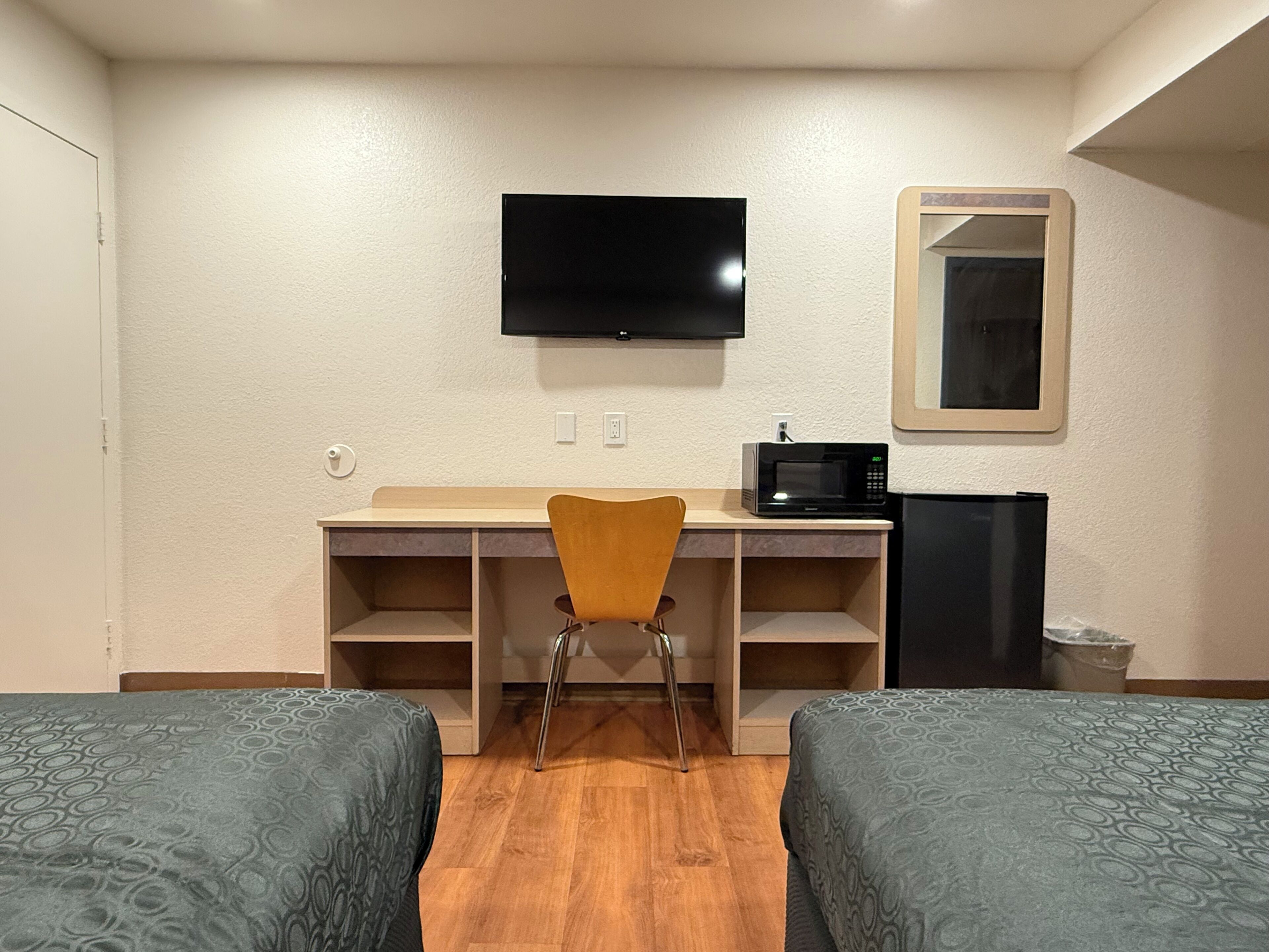 Une chambre d’hôtel avec deux lits, un bureau avec une chaise, une télévision, un four à micro-ondes et une poubelle.