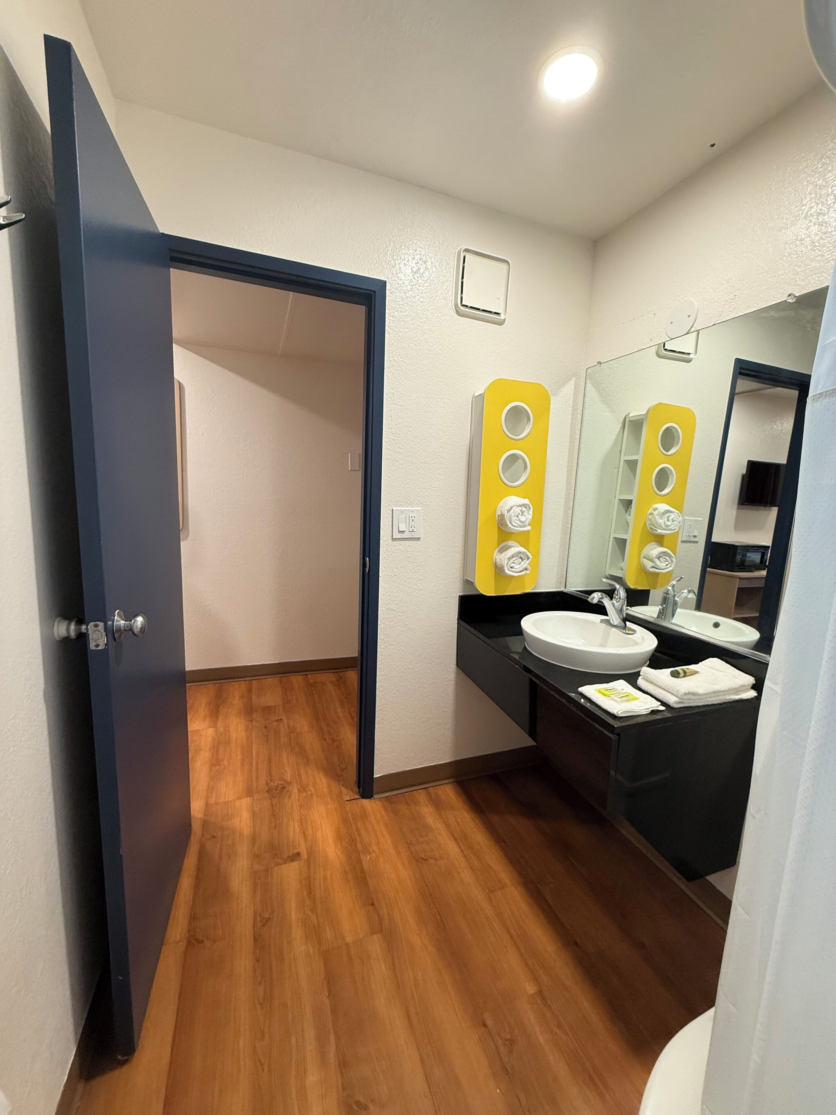 A bathroom with a wooden floor, a white sink, a mirror, and a yellow towel rack.