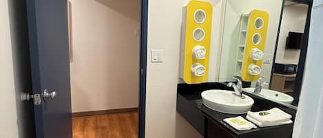 A bathroom with a wooden floor, a white sink, a mirror, and a yellow towel rack.