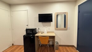 Habitació compacta amb microones, taula petita, cadira, televisió i mirall a la paret.