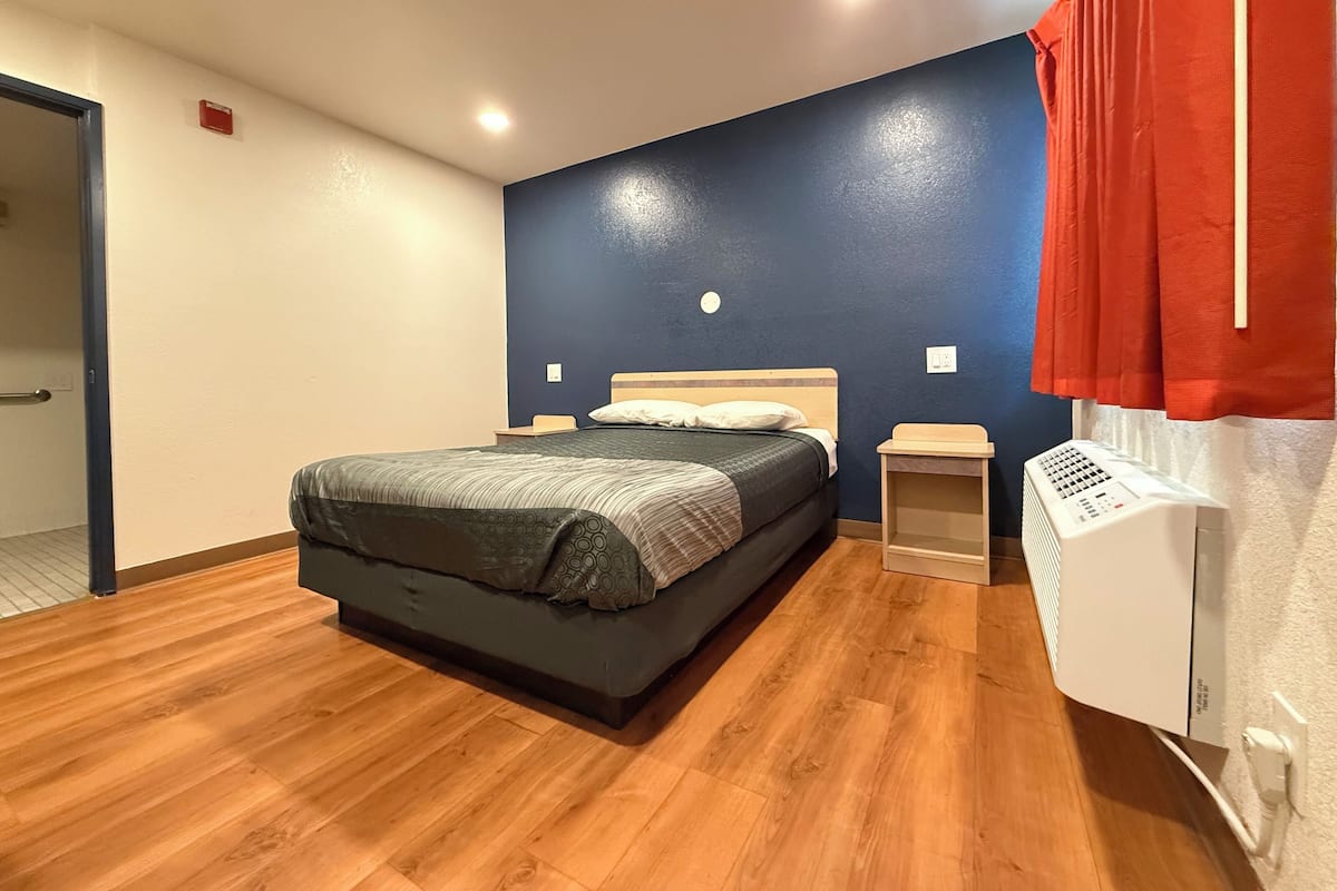 A bedroom with a bed, wooden flooring, a heater, and a blue accent wall.