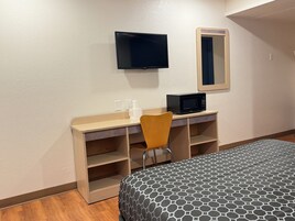 Habitación de hotel con cama, escritorio con silla, televisor, microondas y espejo.