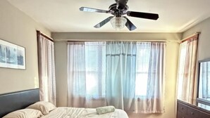 A bedroom with a bed, a ceiling fan, a dresser, and a window with curtains.