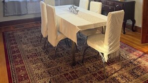 A dining room with a table set for six, surrounded by six chairs, a chandelier, and a large window with curtains. - 3-bedroom apartment in charming St. Louis with close to many attractive places. (St. Louis)
