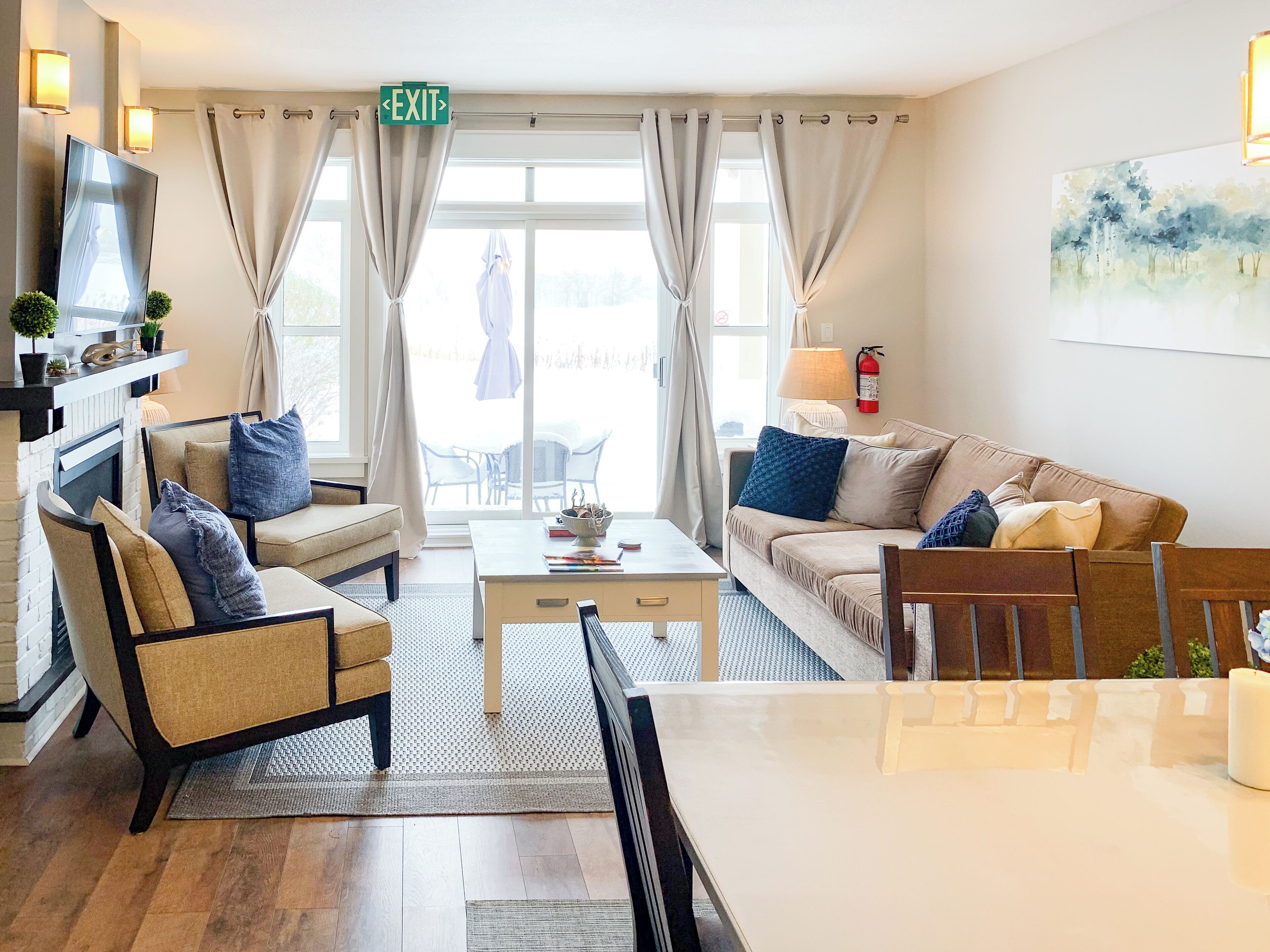 A modern living room with a fireplace, comfortable seating, a coffee table, and a view of the outdoors.