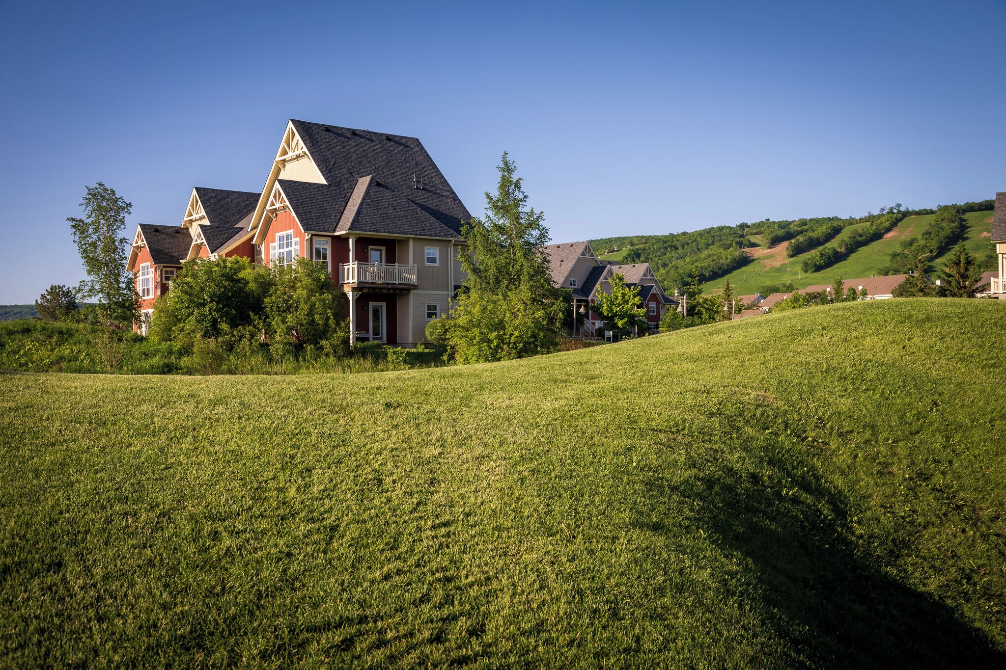 A large house with a balcony, surrounded by a grassy field and trees.
