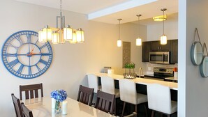 A modern dining area with a large wall clock, a chandelier, and a kitchen in the background. - 3 Peaks at Blue Mountains, your luxury staycation! (The Blue Mountains)