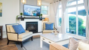 A living room with a fireplace, two sofas with blue cushions, a coffee table, and a TV mounted above the fireplace. - 3 Peaks at Blue Mountains, your luxury staycation! (The Blue Mountains)