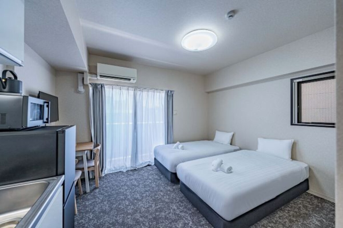 Quarto de hotel com duas camas, uma escrivaninha com cadeira, micro-ondas e ar condicionado.
