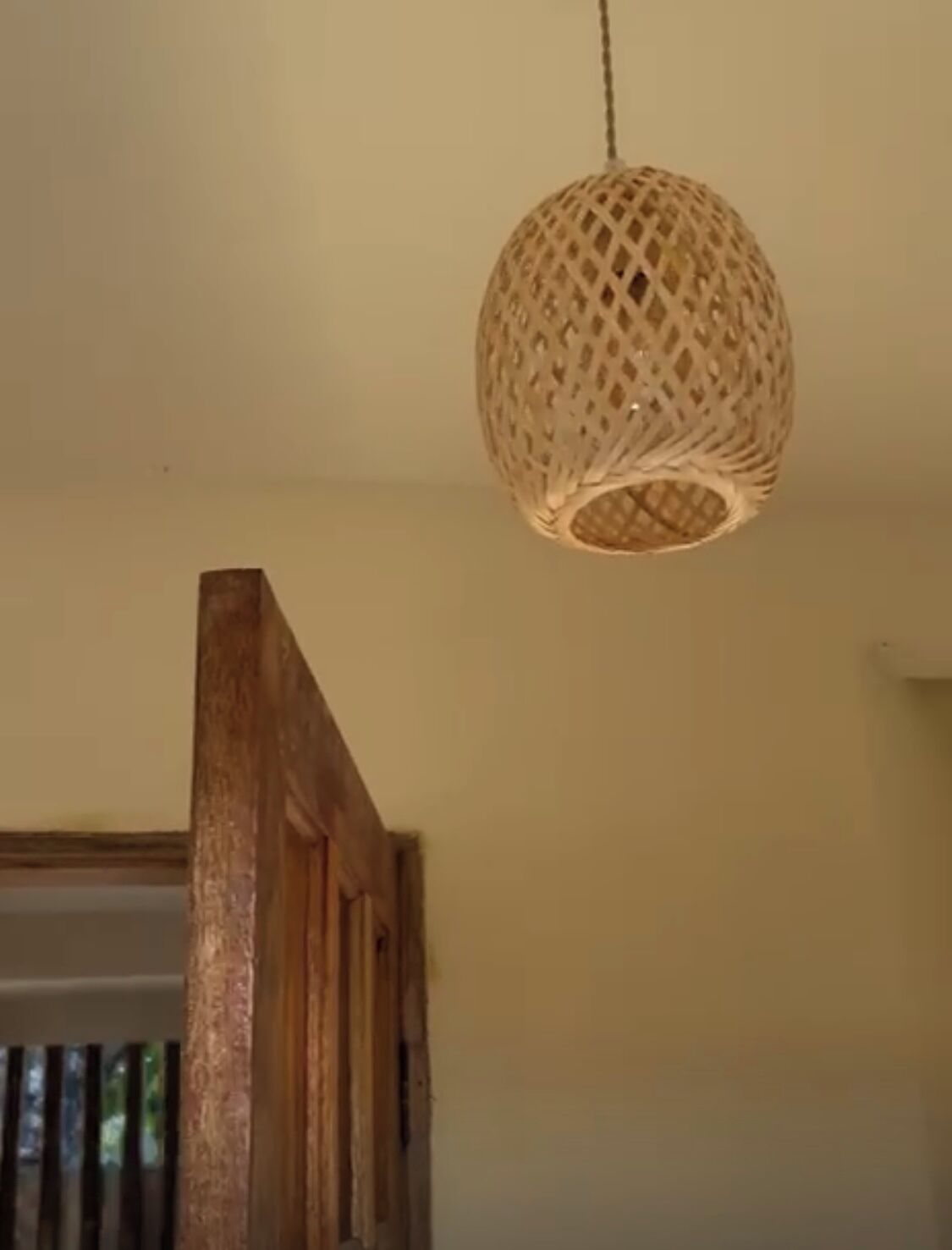 Une pièce dotée d’un escalier en bois et d’un luminaire suspendu en fibres tressées.