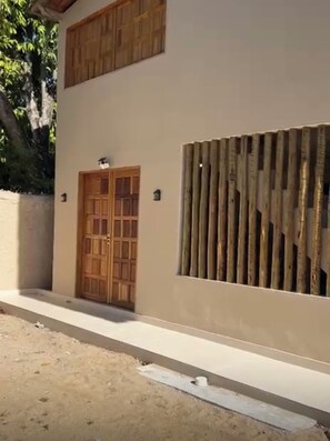 Un bâtiment doté d’une porte en bois, d’une grande fenêtre avec des stores verticaux et d’un sol en béton.
