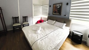 Un dormitorio con una cama grande, dos sillas, un cuadro en la pared y una ventana con persianas.