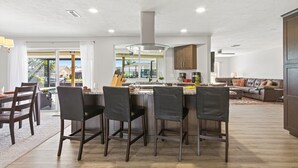 Cozinha moderna com ilha central, cadeiras escuras e área de refeições com mesa e cadeiras.