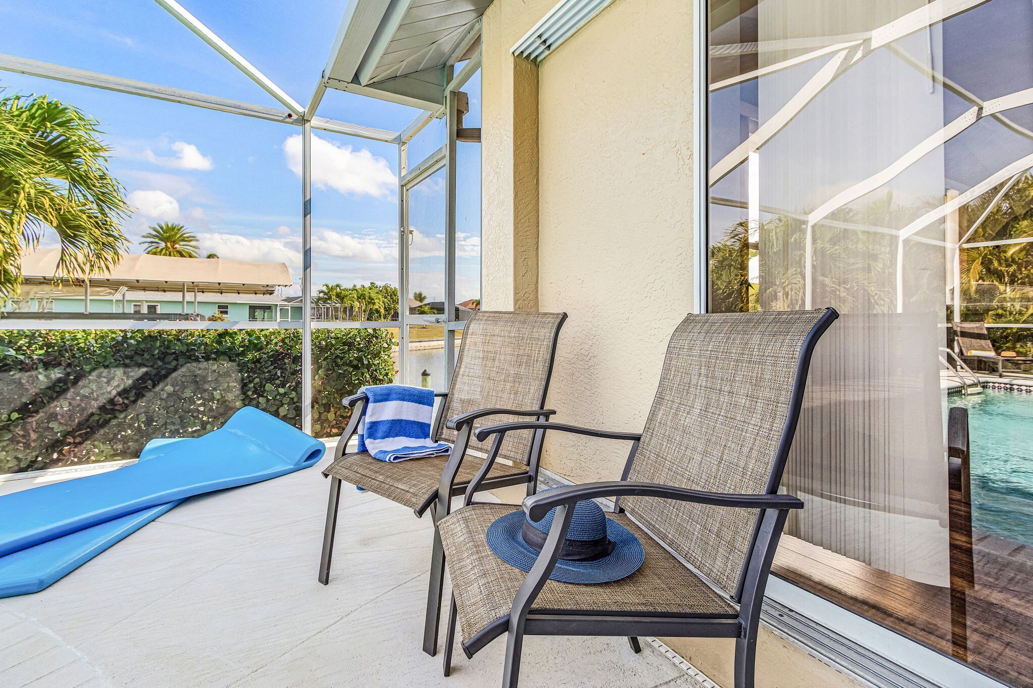 A covered outdoor area with two lounge chairs, a blue mat, and a pool view.