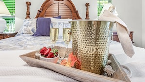 A bed with a wooden headboard, a tray with champagne glasses, strawberries, and a decorative bucket. - Gulf Access, Heated Pool, Bikes- Coastal Breeze - Roelens Vacations (Cape Coral)