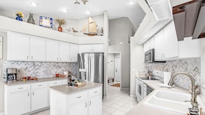 A modern kitchen with white cabinets, a stainless steel refrigerator, and a herringbone tile backsplash. - Gulf Access, Heated Pool, Bikes- Coastal Breeze - Roelens Vacations (Cape Coral)