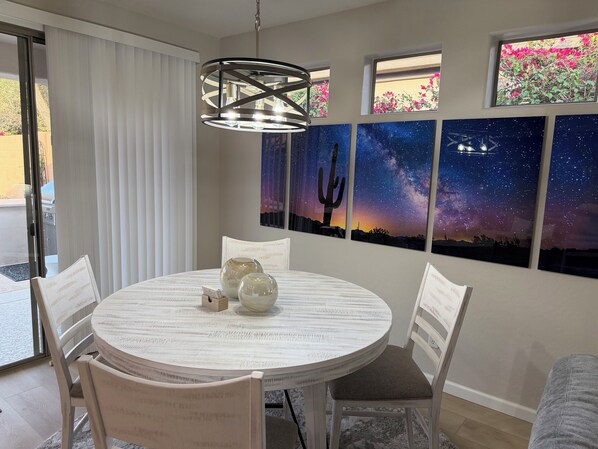 Un comedor con una mesa redonda, sillas blancas, una lámpara colgante moderna y una pared con tres cuadros de noche estrellada.