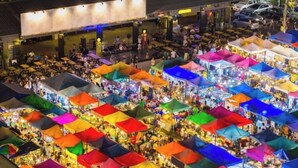 Un marché couvert avec de nombreux étals abrités sous des parasols colorés, entouré d’une galerie couverte et d’un bâtiment à toit plat.