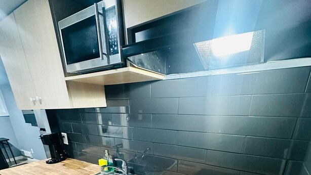 A modern kitchen with a wooden countertop, stainless steel sink, and a black induction cooktop. - Sky Cove | Skyline + River Vibes (Windsor)