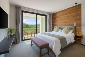 Habitación de hotel moderna con una cama grande, un banco, un televisor y vistas a un paisaje verde.