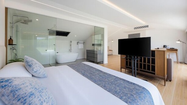 A modern hotel room with a large bed, a TV, a desk, and a glass-enclosed bathroom. - Yashi Mountain Stream · Children's Swimming Pool Designer Parent Child Vacation Scenic Stay (Hangzhou)