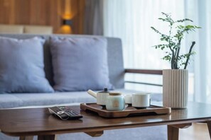 A wooden coffee table with a remote control, a teapot, and cups, a potted plant, and a sofa with cushions in a room with wooden walls and a window. - Yashi Mountain Stream · Children's Swimming Pool Designer Parent Child Vacation Scenic Stay (Hangzhou)