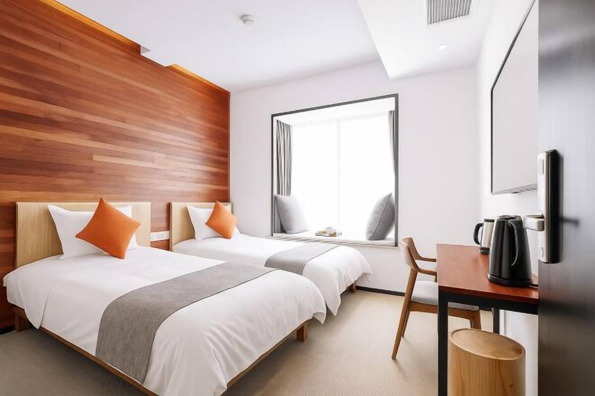 Habitación de hotel con dos camas, un ventanal grande, un escritorio con hervidor y un cubo de basura.