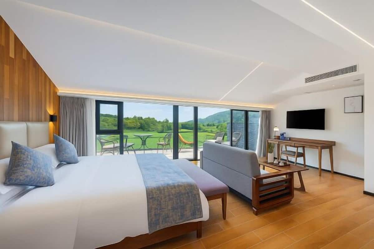 Una habitación de hotel moderna con una cama grande, un sofá, un escritorio y una televisión. La habitación tiene un ventanal con vistas a un campo de golf.