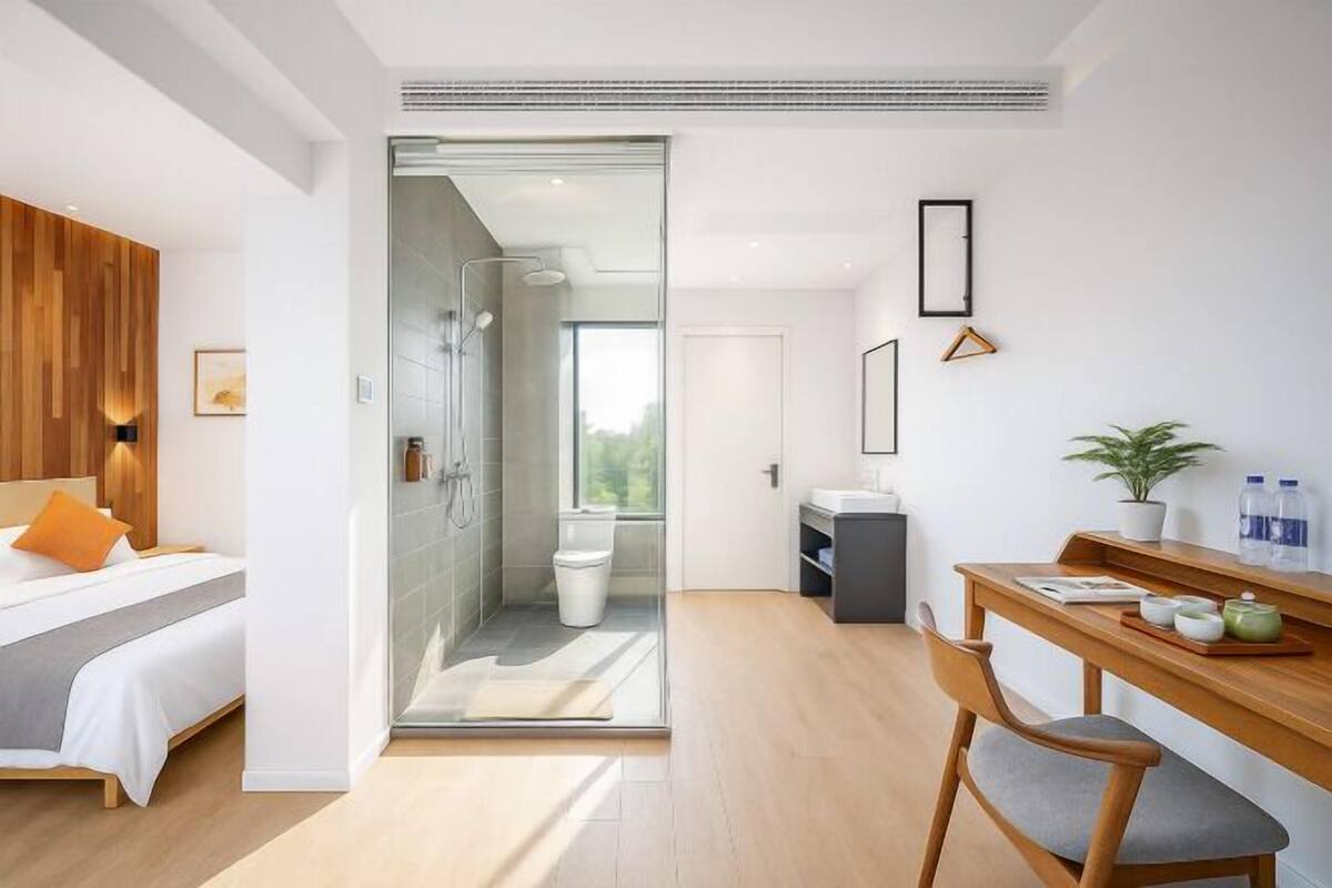 Habitación de hotel moderna con cama, escritorio, silla, zona de ducha y vistas al exterior.