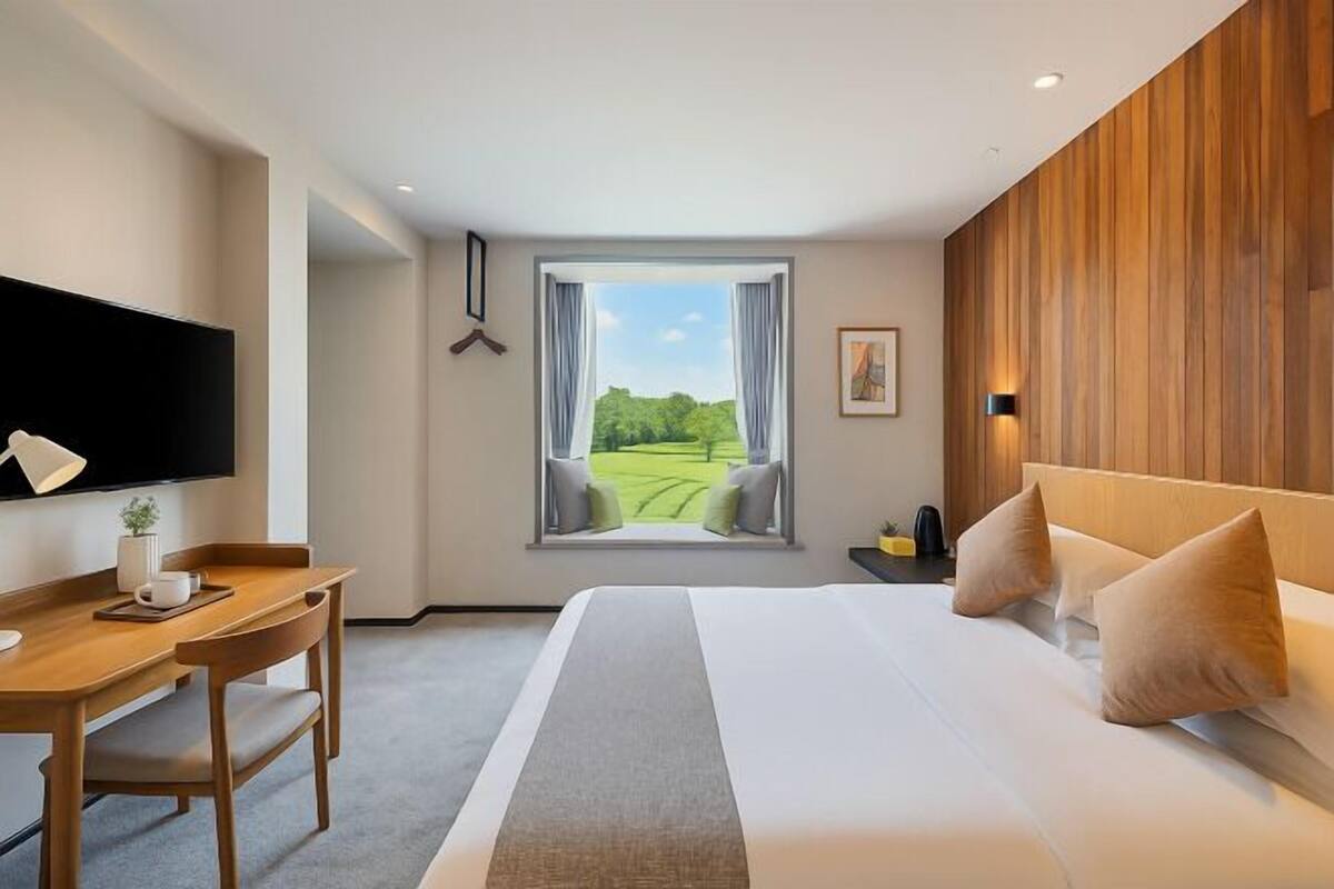 Habitación de hotel con una cama grande, un escritorio con silla, un televisor de pantalla plana, un ventanal con vistas a zonas verdes y una pared de acento de madera.