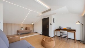 A modern, well-lit room with a wooden floor, a sofa, a desk with a chair, and a black door. - Yashi Mountain Stream · Children's Swimming Pool Designer Parent Child Vacation Scenic Stay (Hangzhou)