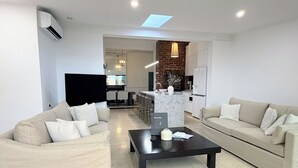 A modern living room with two sofas, a coffee table, a TV, and a kitchen area visible in the background. - Perfect North Adelaide Location. Walk everywhere! (North Adelaide)