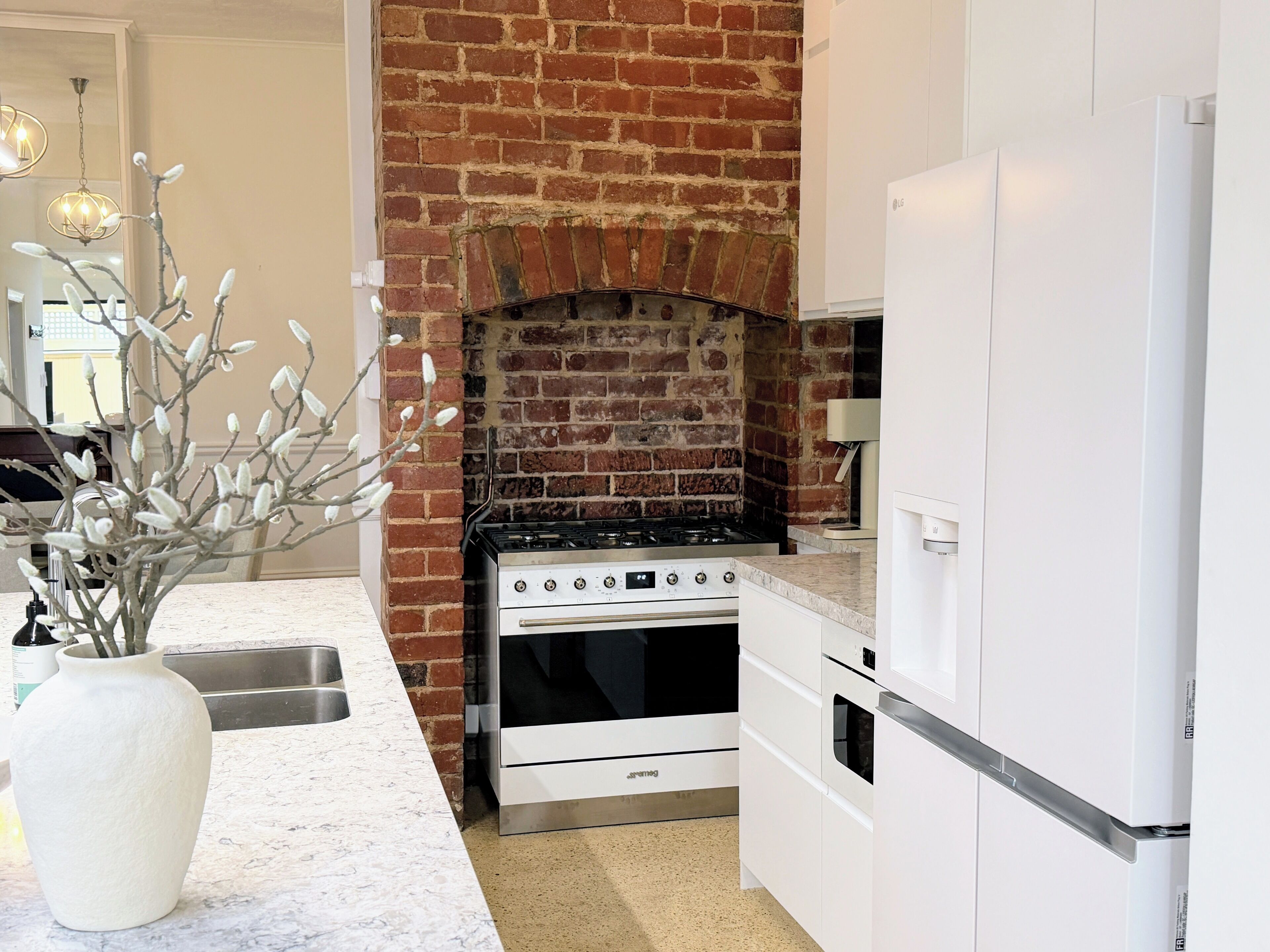 A kitchen with a brick wall, a gas stove, a built-in oven, and a white refrigerator.