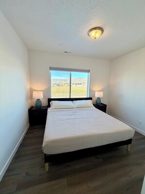 A bedroom with a large bed, two bedside lamps, a window with a view, and a ceiling light.
