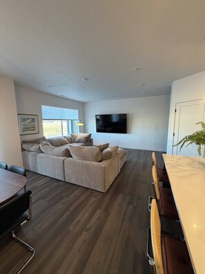 A modern living room with a sectional sofa, a flat-screen TV, and a dining area with a table and chairs.